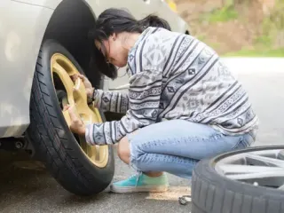 Woman changing a tire on the side of the street