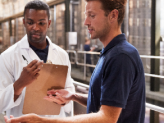 man in lab coat talking to worker